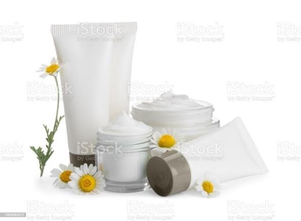 Cosmetic products including white tubes and jars with cream, arranged with fresh daisy flowers on a white background, suggesting natural skincare products.